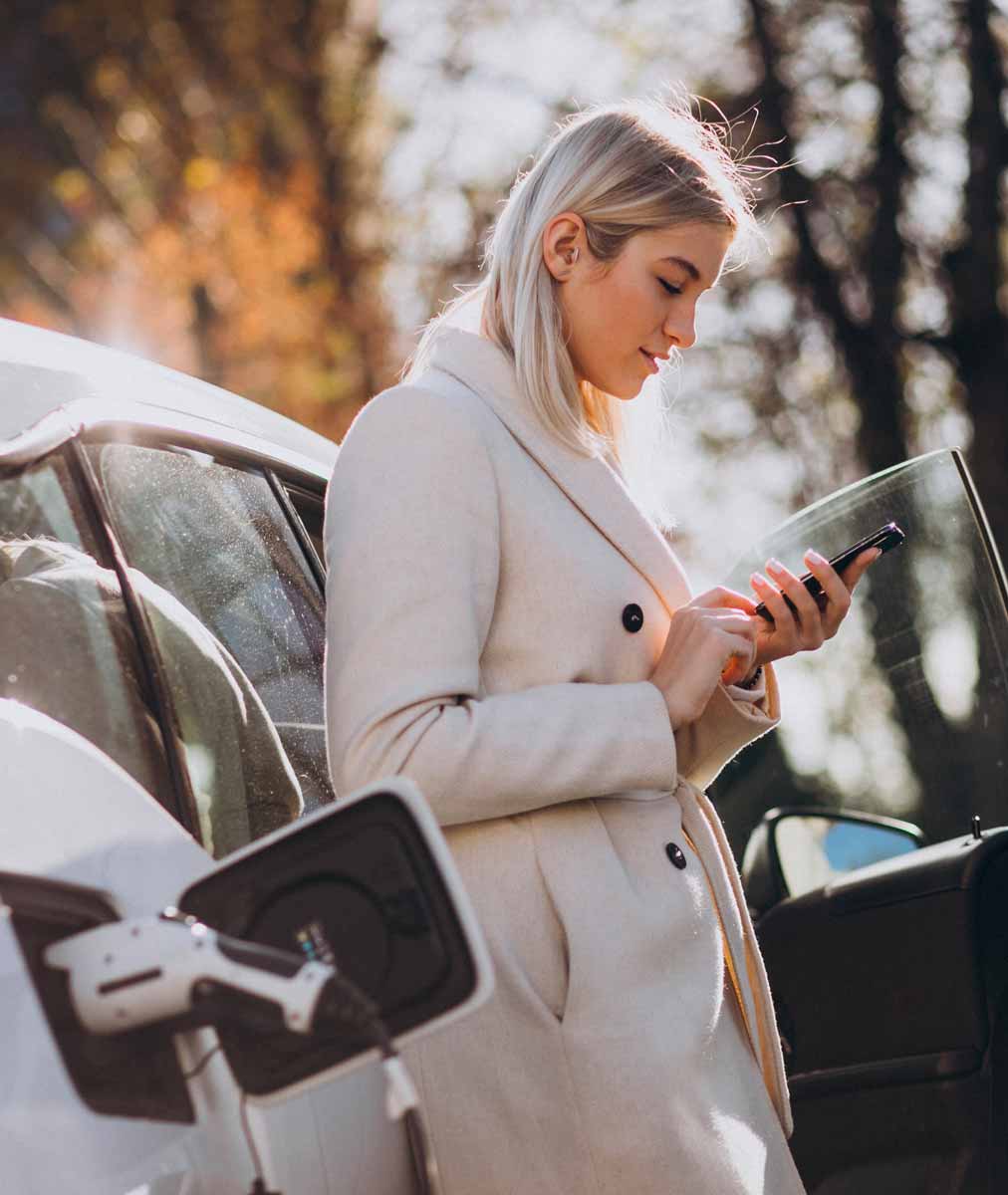 Immagine di donna con smartphone che sta ricaricando auto da colonnina di ricarica
